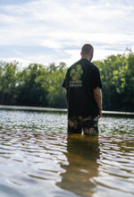 Load image into Gallery viewer, man wearing green oversized DFKT Fruits t-shirt showing back graphic standing in a lake