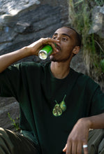 Load image into Gallery viewer, man wearing green oversized DFKT Fruits t-shirt showing front graphic sipping energy drink