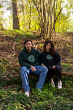 Load image into Gallery viewer, man wearing green oversized tree of life hoodie with woman wearing black oversized tree of life t-shirt in the forest