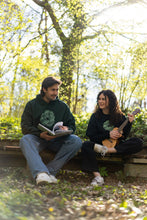 Load image into Gallery viewer, man wearing oversized green tree of life graphic hoodie while sketching, woman wearing black oversized tree of life t-shirt while playing a banjo