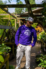 Load image into Gallery viewer, man wearing purple eye bubbles relaxed sweater with white linen pants and a white cap in a greenhouse