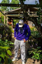 Load image into Gallery viewer, man wearing purple eye bubbles relaxed sweater with white linen pants in a greenhouse