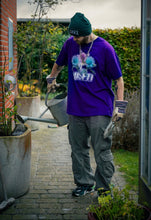 Load image into Gallery viewer, man wearing purple oversized misfit v2 graphic t-shirt with green roboflower cargos and green DFKT logo beanie and puma rs-x while watering plants