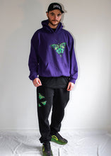 Load image into Gallery viewer, man wearing black ripped butterfly sweatpants with oversized purple ripped butterfly hoodie and black DFKT logo dad hat cap