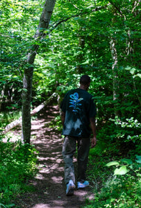 man wearing a green oversized thermal graphic overload t-shirt with air max 98s walking in the forest