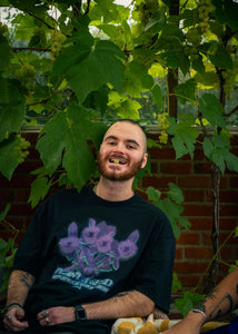 man wearing black oversized Plant A Seed floral graphic t-shirt while eating grapes