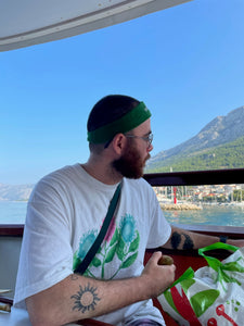 man wearing white misfit t-shirt on a yacht with green halara headband