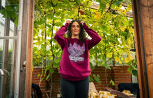 Load image into Gallery viewer, woman wearing oversized maroon plant a seed floral graphic sweater in a green house