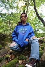Load image into Gallery viewer, Woman wearing oversized blue Human Nature graphic hoodie with blue jeans
