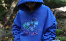 Load image into Gallery viewer, Woman wearing oversized blue Human Nature graphic hoodie with the hoodie up