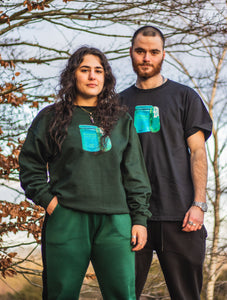 man wearing a black oversized panic control t-shirt and woman wearing a green panic control sweater