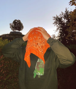 man wearing a green cozy fit think outside the jar sweater with orange bandana on his head