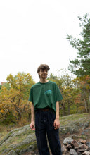 Load image into Gallery viewer, man wearing green oversized mindliquid logo t-shirt with dark blue jeans