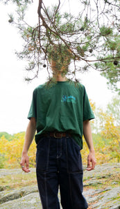 man wearing green oversized mindliquid logo t-shirt with tree branch covering his face
