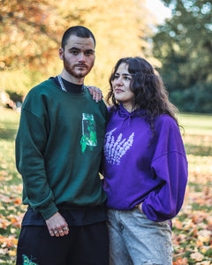 man wearing green oversized think outside the jar cozy sweater and black ripped butterfly sweatpants with woman wearing oversized purple lavender hoodie