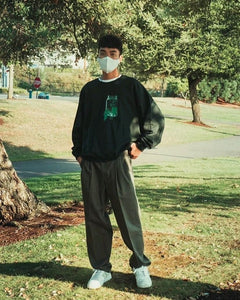 man wearing oversized green think outside the jar graphic sweater with corona mask and baggy earth tone pants