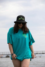 Load image into Gallery viewer, woman wearing oversized green no luck t-shirt with bucket hat