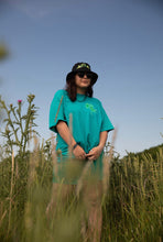 Load image into Gallery viewer, woman wearing oversized green no luck t-shirt with bucket hat in a field of wheat
