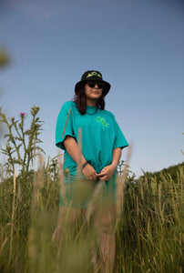 woman wearing oversized green no luck t-shirt with bucket hat in a field of wheat