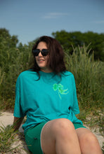 Load image into Gallery viewer, woman wearing oversized green no luck t-shirt with green shorts at the beach